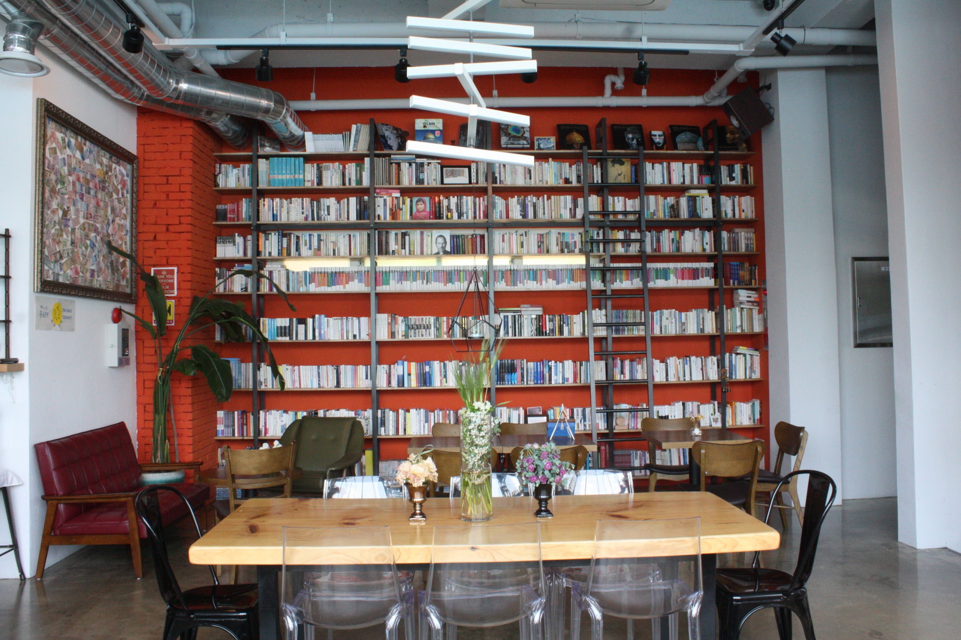 A library with bookshelves, a wooden table, chairs, and a red brick wall.