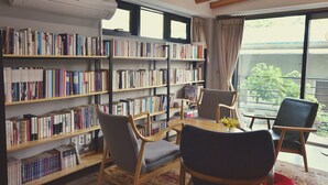 Een kamer met een grote boekenkast vol boeken, een houten tafel met stoelen, en uitzicht op groen buiten.