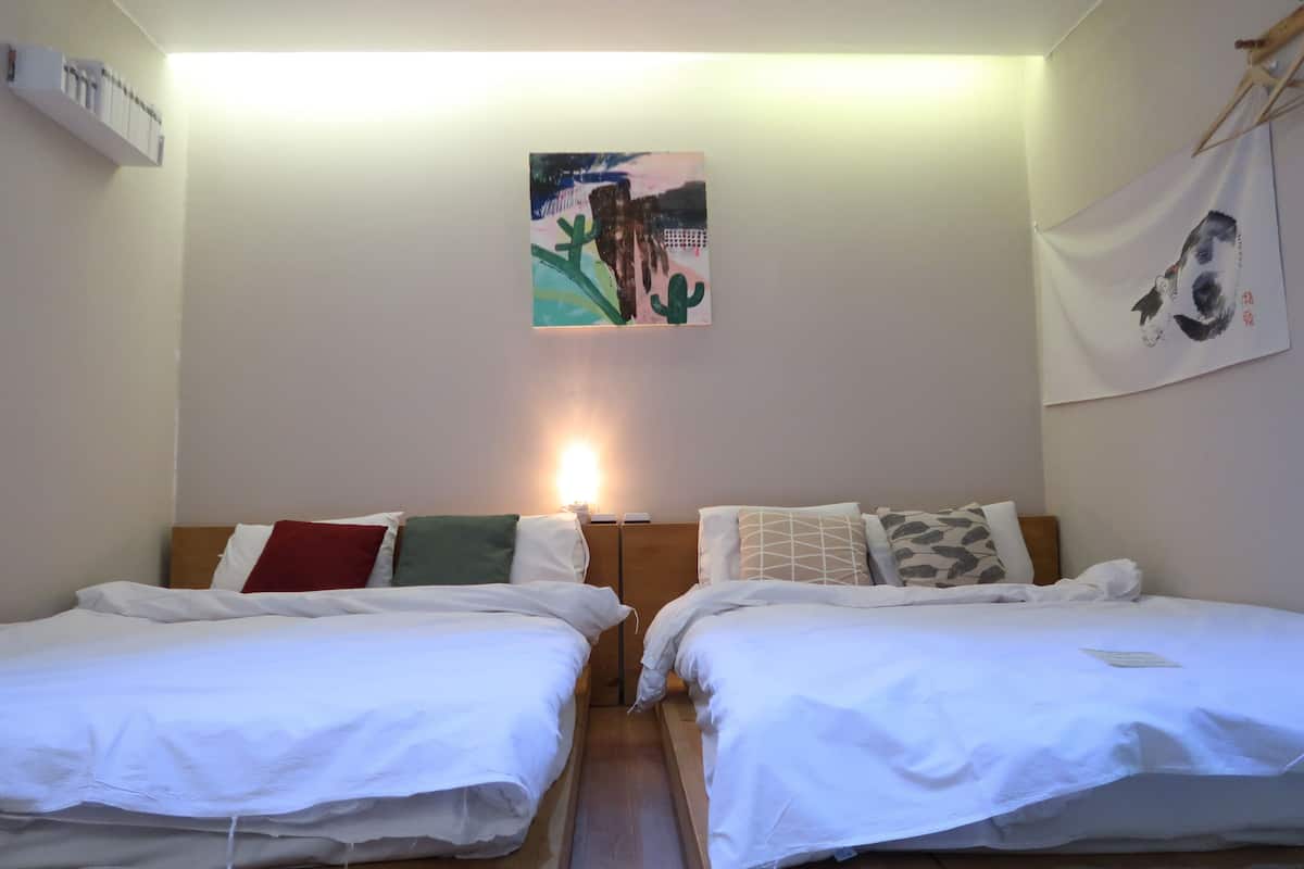 A room with two beds, a wall-mounted artwork, and a ceiling light.