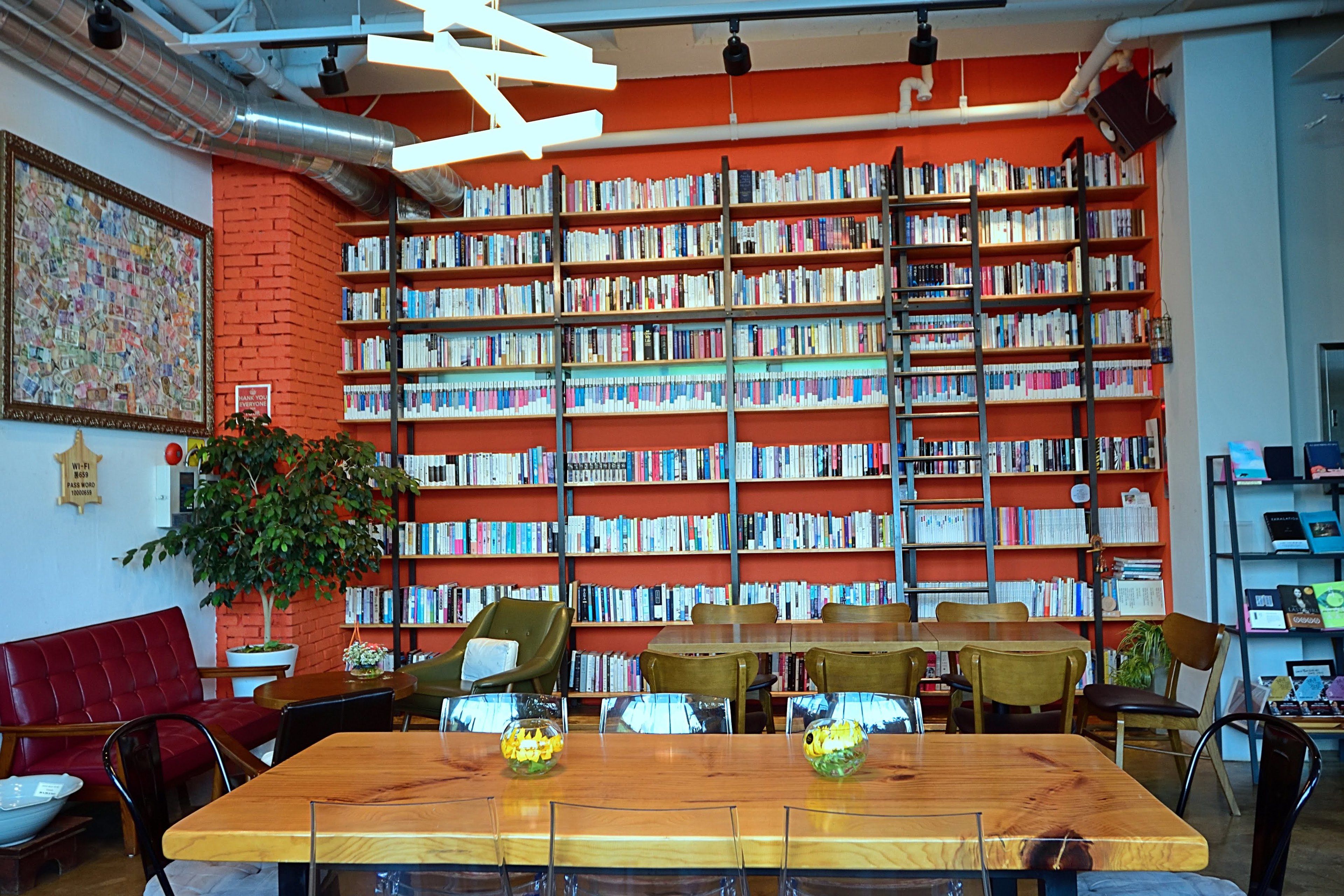 Una biblioteca con scaffali, un tavolo di legno, sedie e un muro in mattoni rossi.