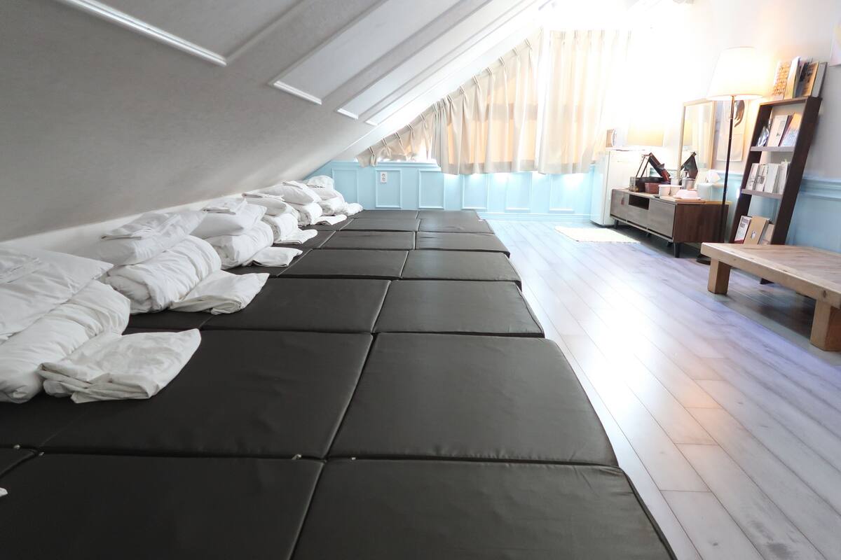 A room with a row of black mattresses, a wooden bench, and a desk with a lamp.