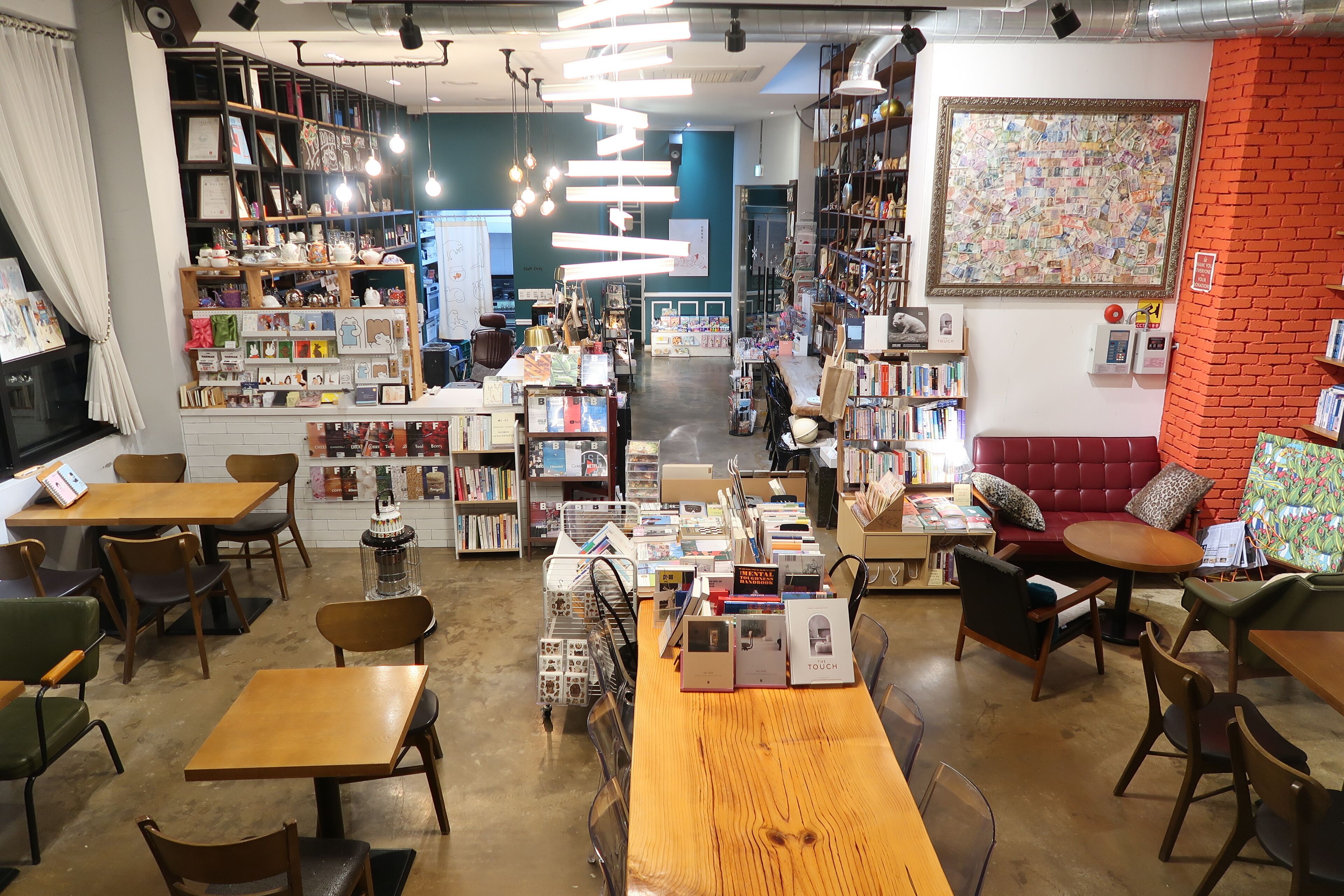 A bookstore with wooden tables and chairs, bookshelves, and a red brick wall.