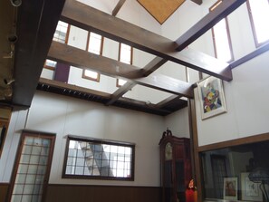 A room with a high ceiling, exposed wooden beams, a large window with a grid pattern, and a traditional wall clock.
