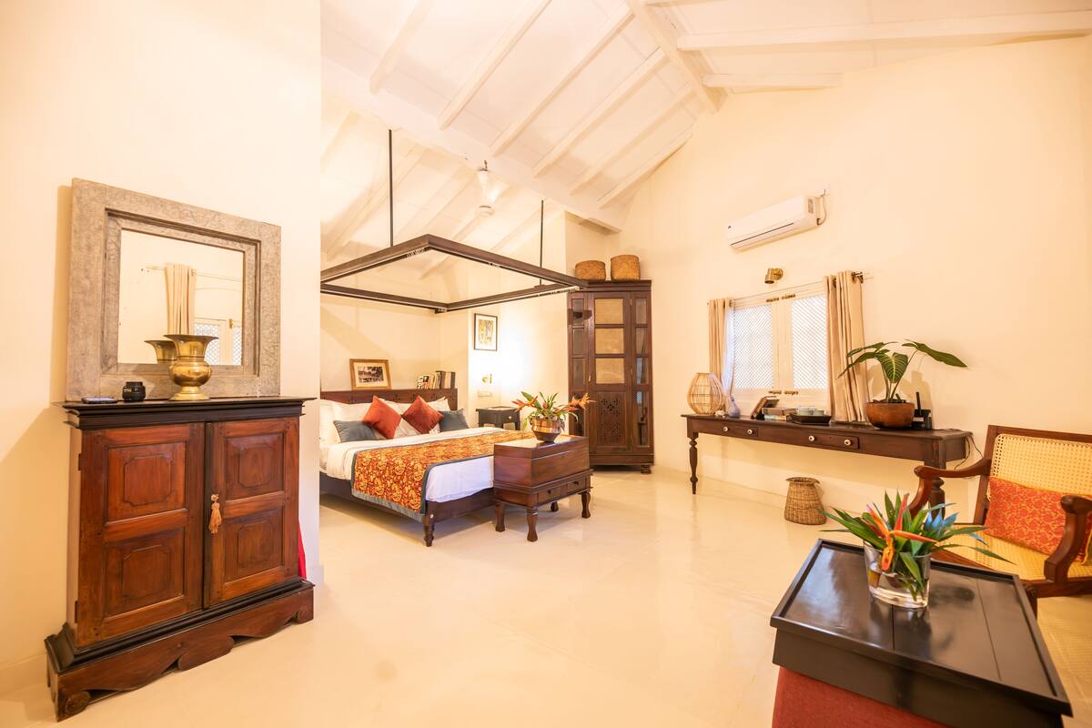 A spacious room with a large bed, a wooden cabinet, a small table, and a chair.