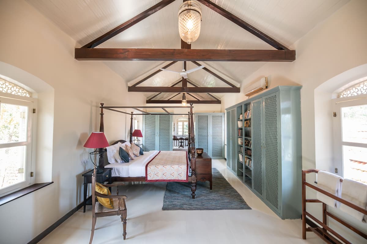 A spacious bedroom with a four-poster bed, a wooden wardrobe, and a large window providing natural light.