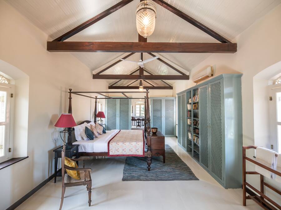 A spacious bedroom with a four-poster bed, a wooden wardrobe, and a large window providing natural light.