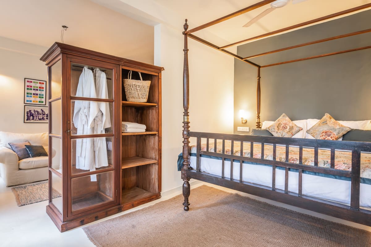 A bedroom with a four-poster bed, a wooden wardrobe, and a large window.