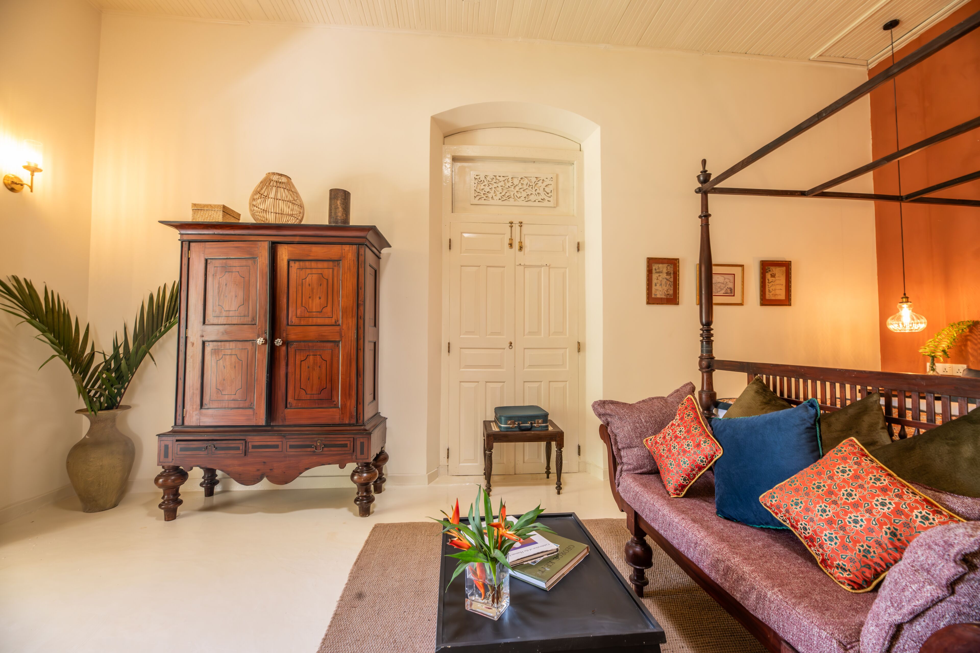A living room with a wooden cabinet, a sofa with patterned cushions, a coffee table with books and a vase, and a door with a decorative panel.
