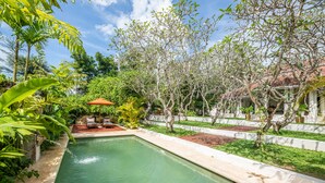 Piscina retangular com céu azul límpido acima, rodeada por vegetação exuberante e um cercado branco.