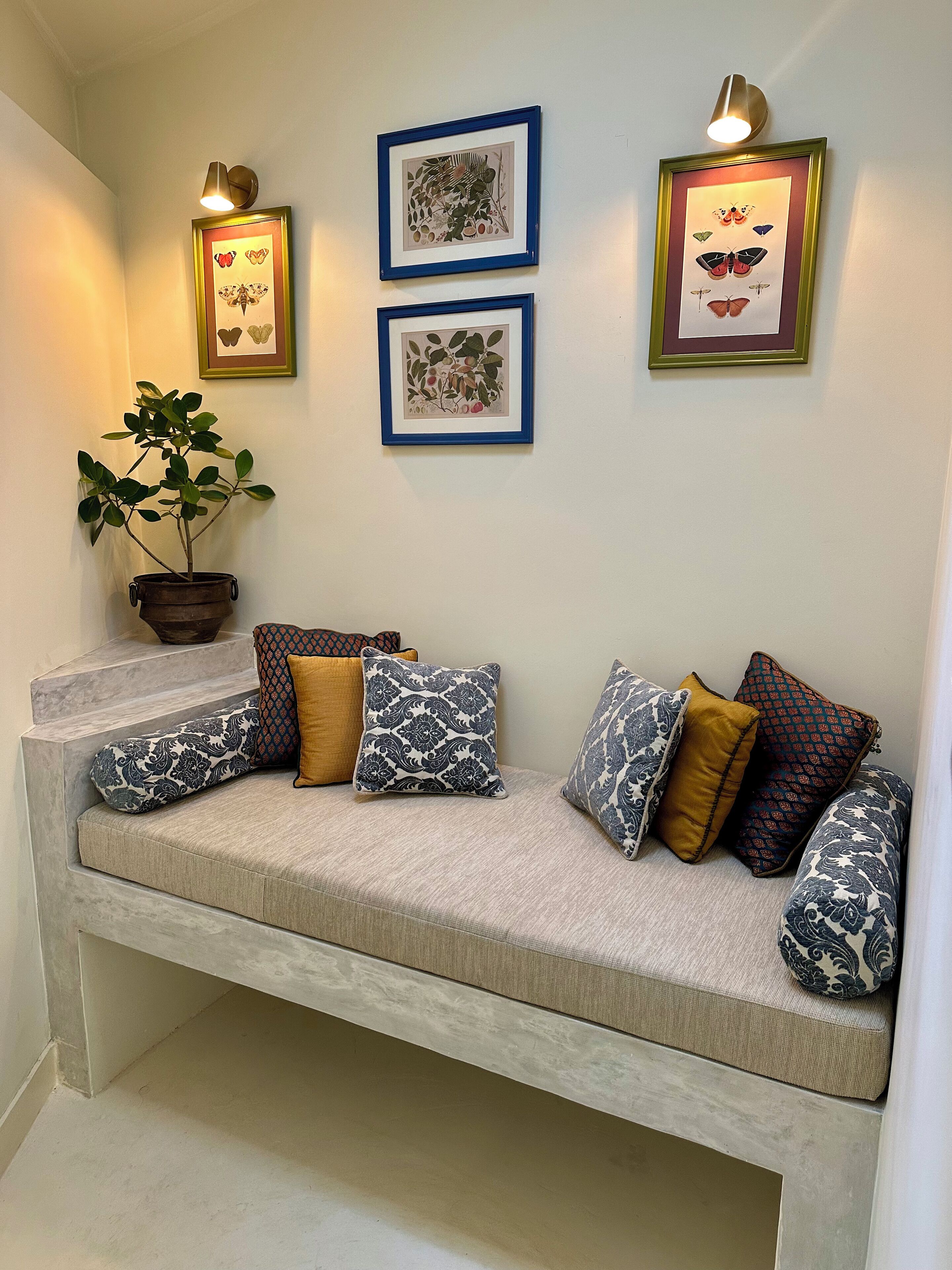 A seating area with a cushioned bench, a potted plant, and framed botanical prints on the wall.