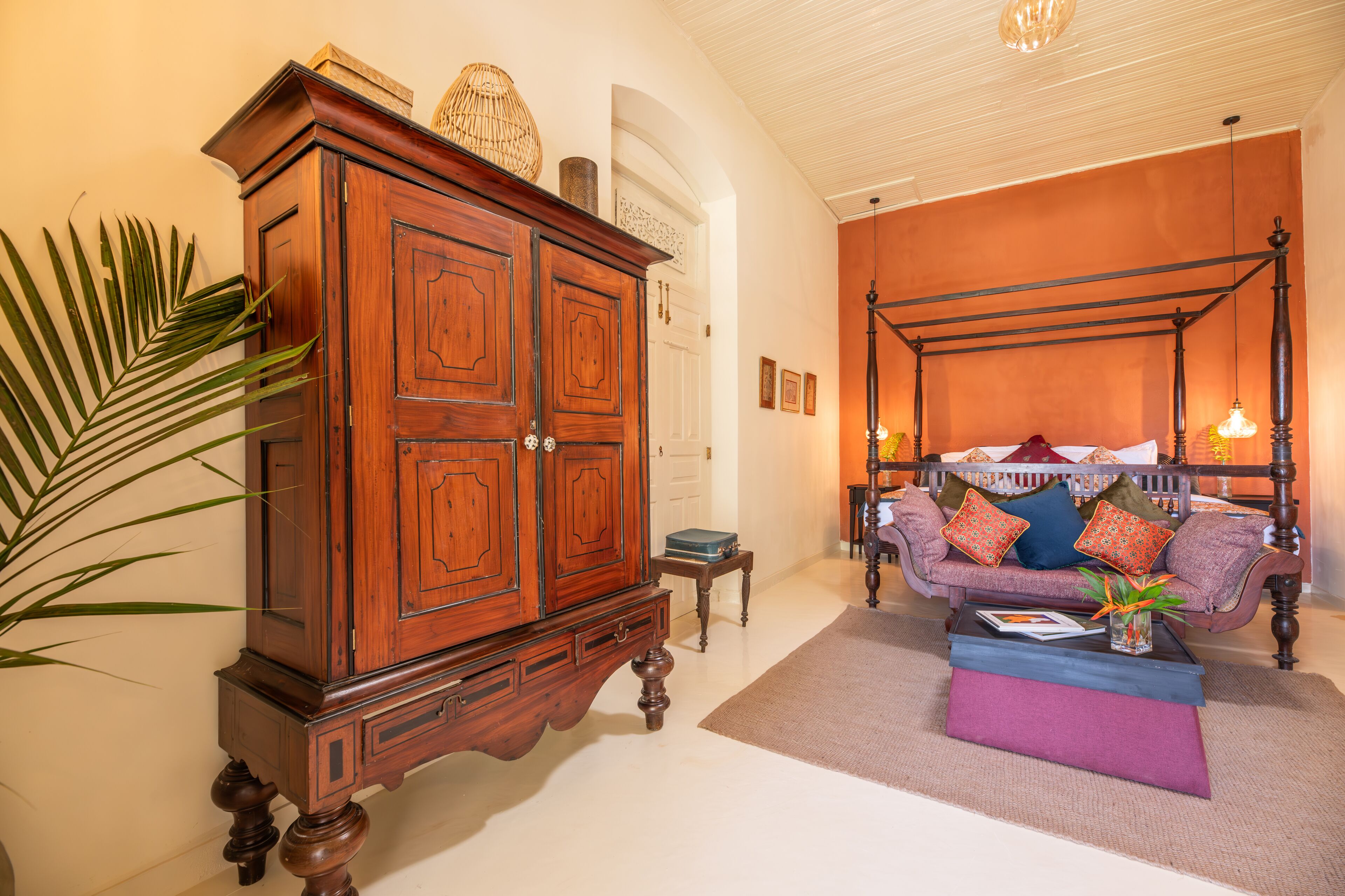 A room with a large wooden cabinet, a four-poster bed, and a small table with a book and a vase.