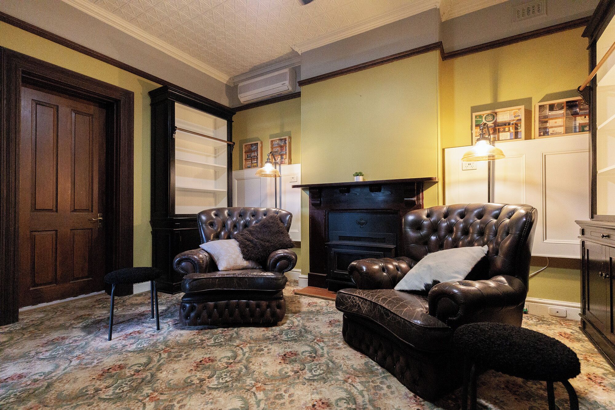 A traditional living room with two leather armchairs, a patterned carpet, a fireplace, and a door.