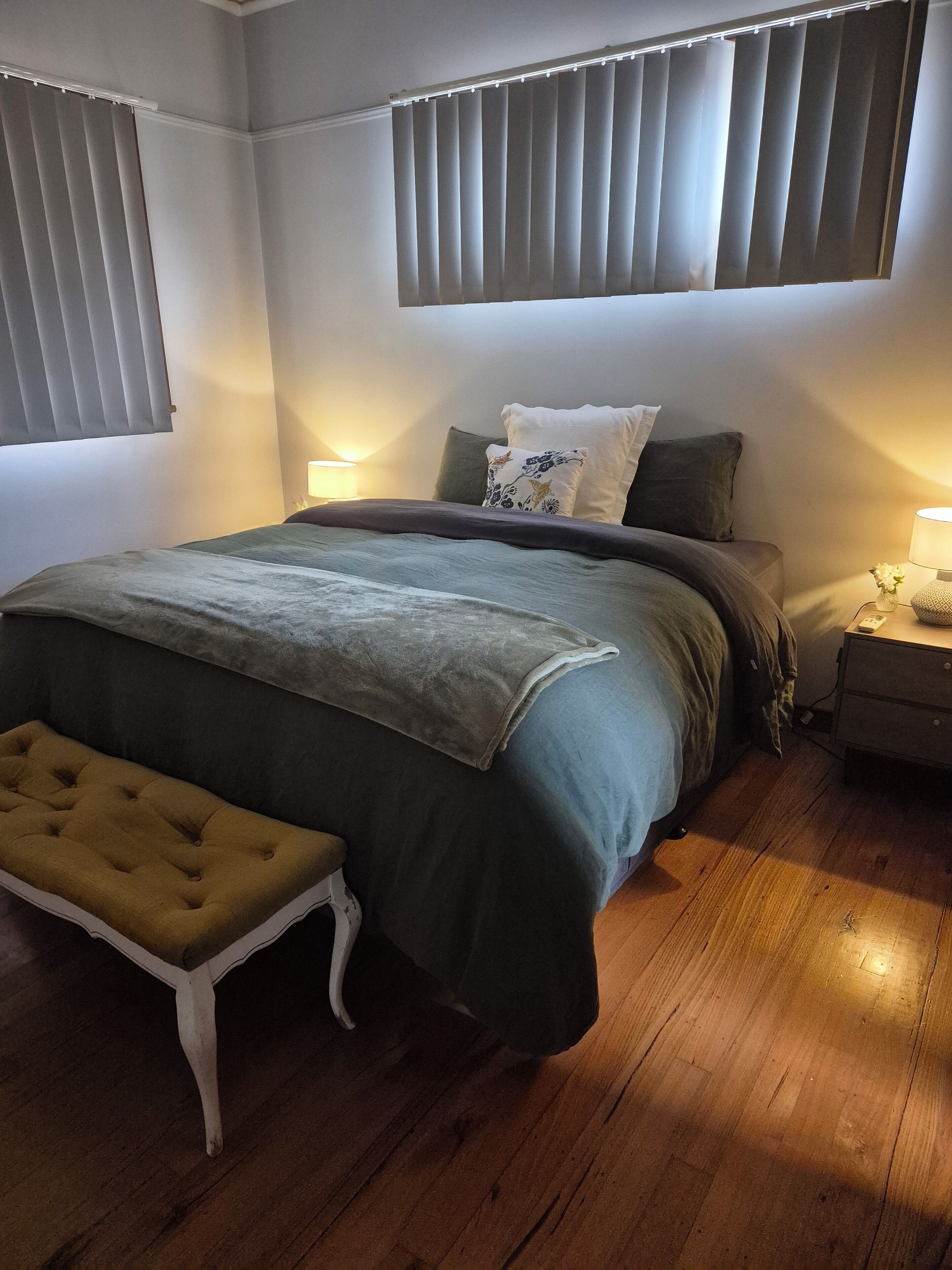 Une chambre à coucher avec un lit, des tables de chevet, un banc et une fenêtre avec des stores.