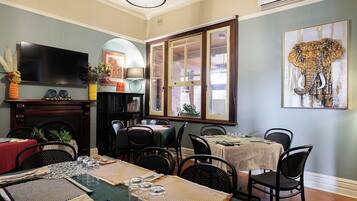 Un comedor con varias mesas dispuestas para una comida, una chimenea, un televisor y un amplio ventanal con vistas.