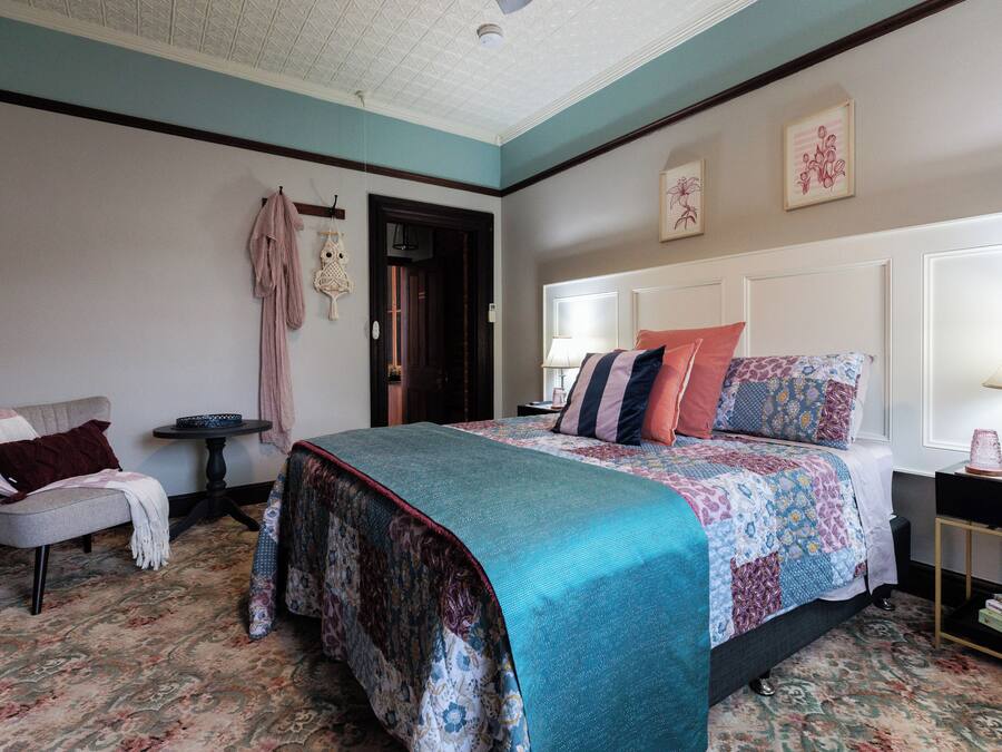 A bedroom with a bed, a chair, a small table, and a nightstand.