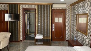 A hotel room with a bed, a chair, a vanity with a mirror, a shower area, and a door with a lock. - Grand Merin Airport Hotel (Istanbul)