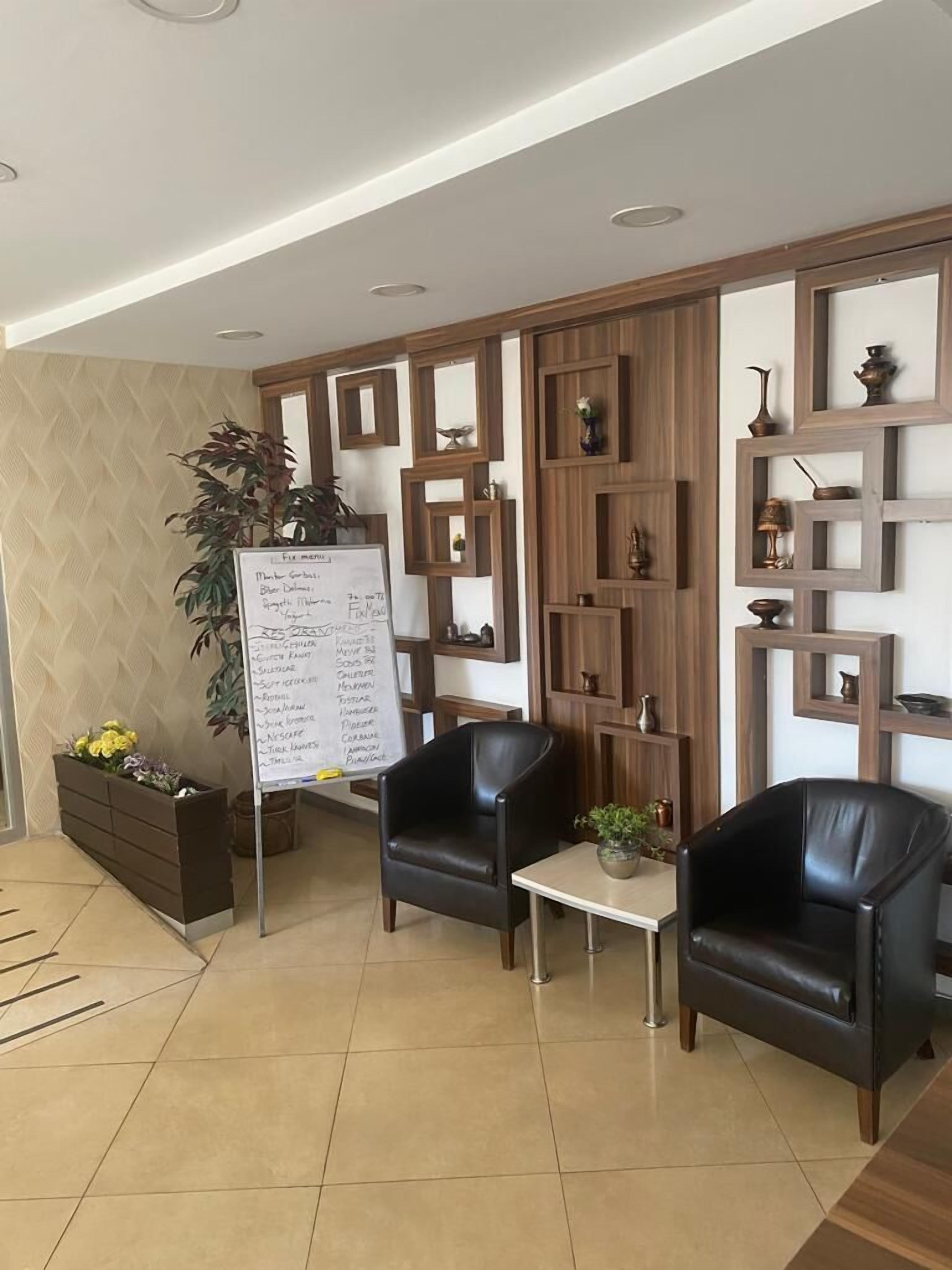 A modern waiting area with two leather chairs, a small table, a whiteboard with a list, and decorative shelves.