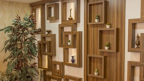 A lobby with wooden shelving units displaying decorative items, leather armchairs, and a coffee table. - Grand Merin Airport Hotel (Istanbul)