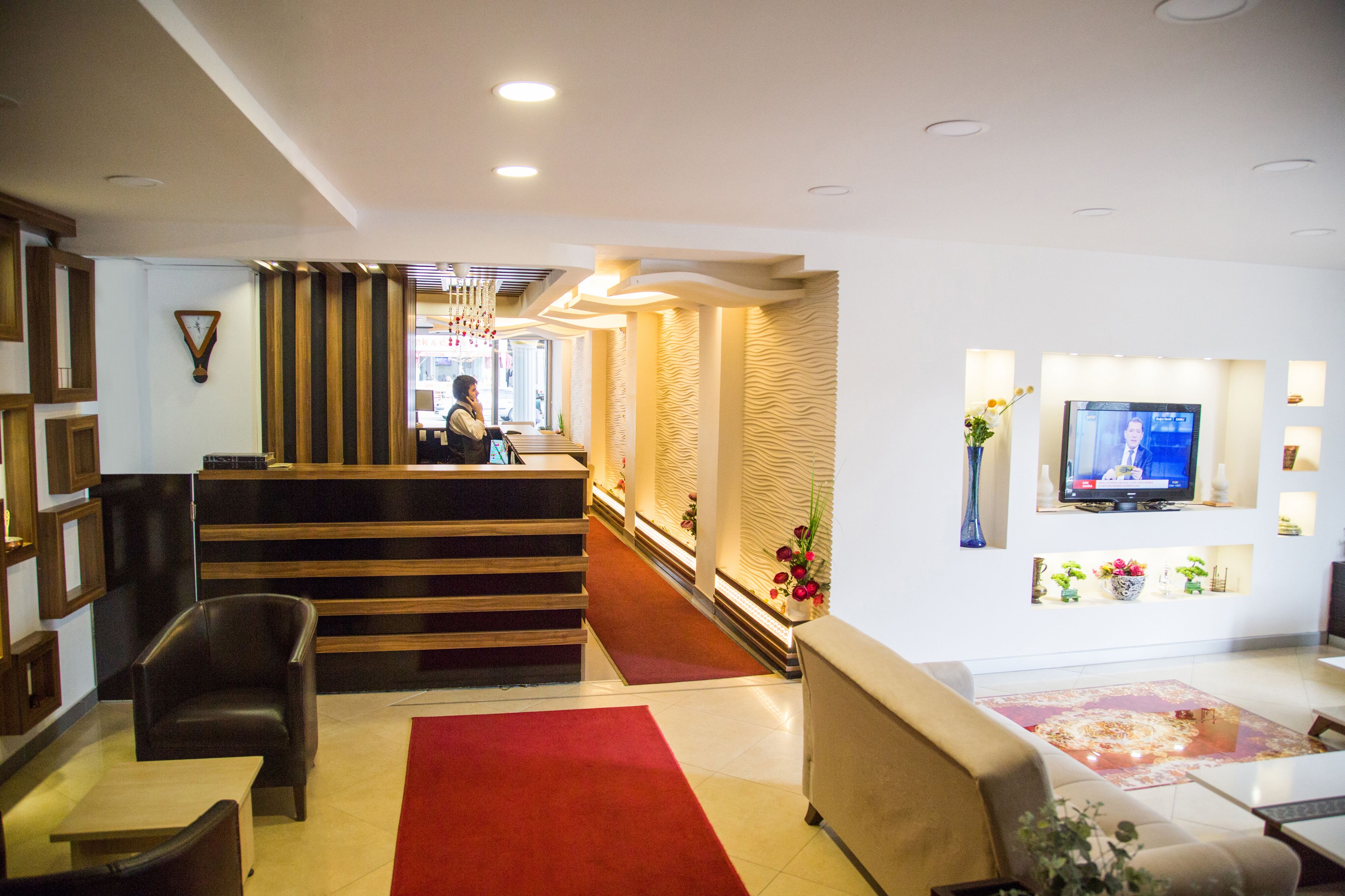 Un vestíbulo de hotel con mostrador de recepción, zona de estar y televisor.