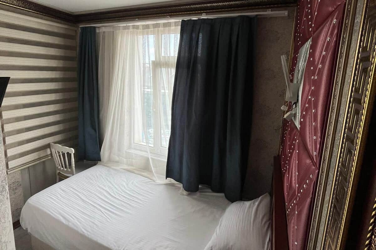 A room with a bed, a chair, a window with curtains, and a mirror with a decorative frame.