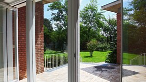 Une porte vitrée donne sur un patio bordé d’un mur en briques et d’une pelouse.