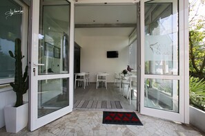 A modern interior with a glass door leading to a dining area with white chairs and a table. - Villa Silvia Olivetti (Banchette)
