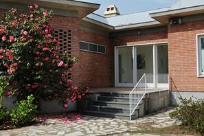 A brick building with a tiled patio, a rose bush, and a staircase leading to a door. - Villa Silvia Olivetti (Banchette)