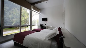 Une chambre moderne avec une grande fenêtre, un lit, une table de chevet et un téléviseur fixé au mur.