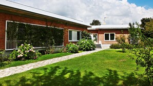 Une maison moderne à deux étages, dotée d’une façade en briques, de grandes fenêtres et d’un jardin bien entretenu avec un chemin.