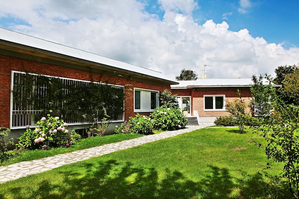 A modern two-story house with a brick facade, large windows, and a well-maintained garden with a pathway.