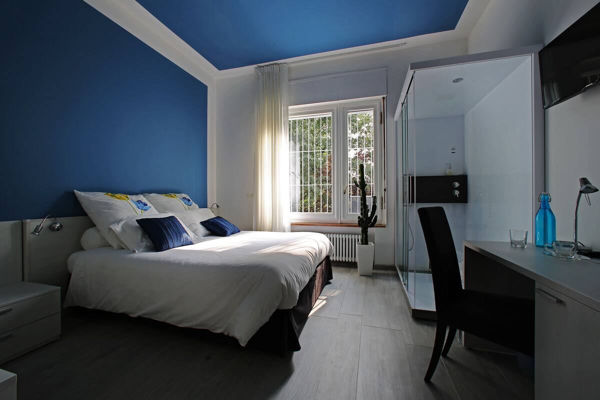 A bedroom with a bed, a desk, a chair, a window, and a radiator.