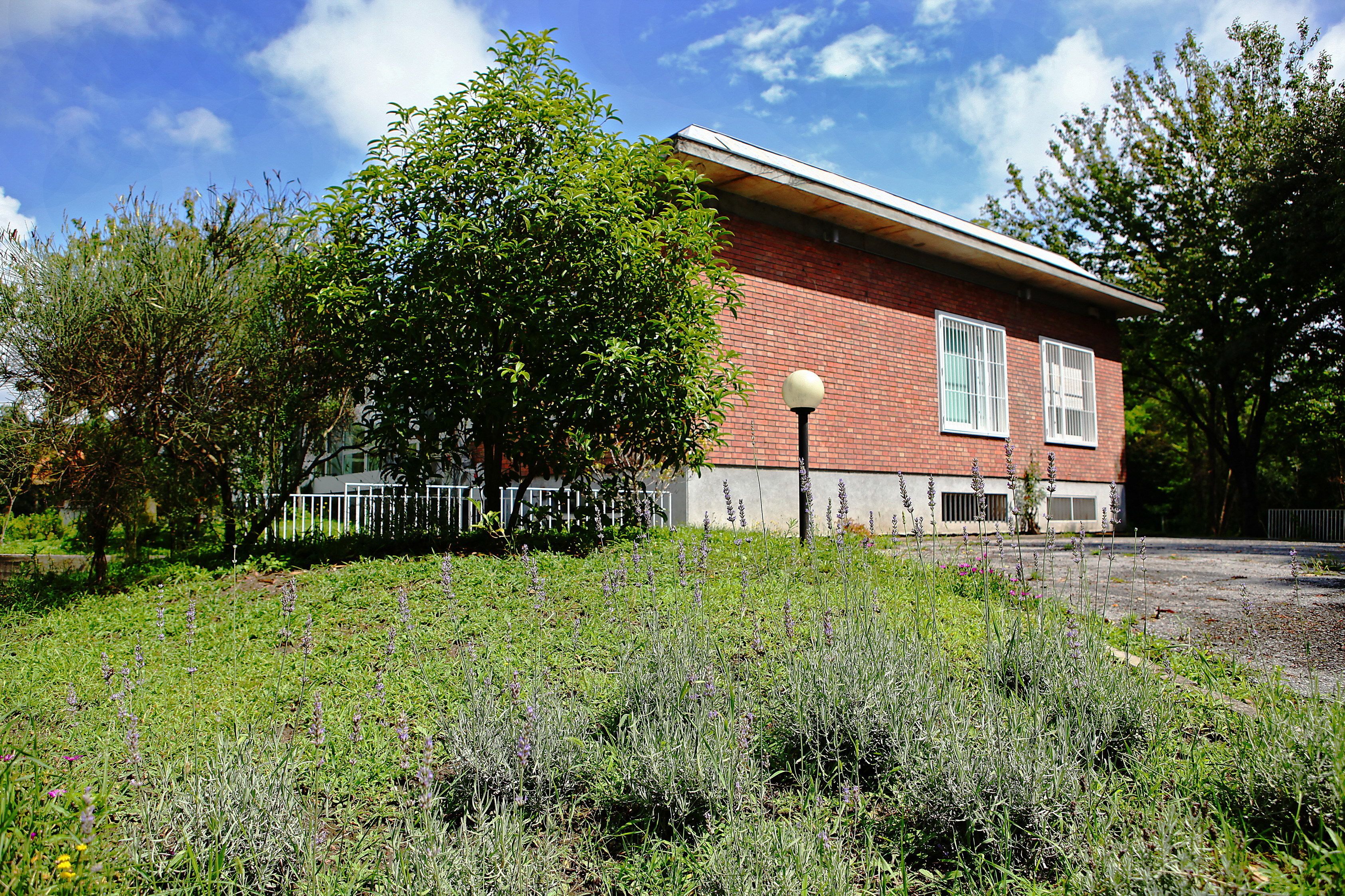 A red brick building with a white fence, surrounded by greenery and a clear sky.