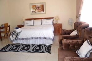 Un dormitorio con una cama grande, una mesita de noche de madera, un sillón marrón y un tapete con estampado blanco y negro.