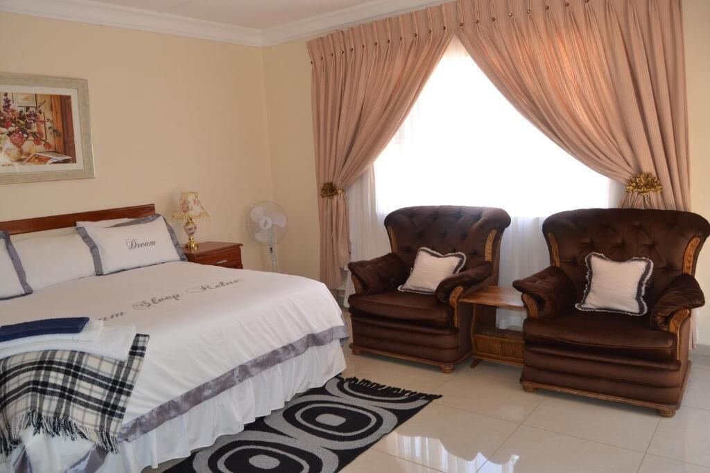 A bedroom with a large bed, two armchairs, a nightstand, a lamp, and a window with curtains.
