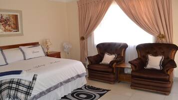 A bedroom with a large bed, two armchairs, a nightstand, a lamp, and a window with curtains.