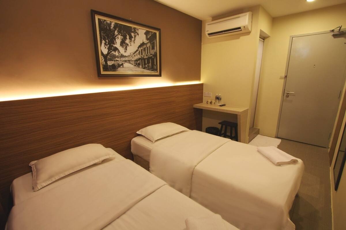 A hotel room with two beds, a small desk with a chair, an air conditioning unit, and a door.