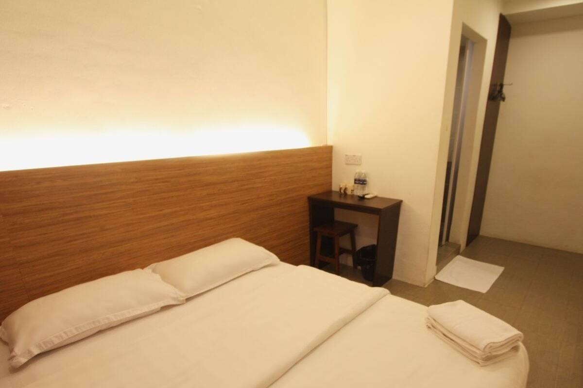 A neatly made bed with white linens, a wooden headboard, a small bedside table with a lamp, and a folded towel on the floor.