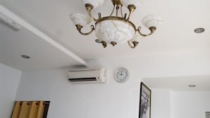 A room with a chandelier, an air conditioning unit, a clock, and a framed picture on the wall.