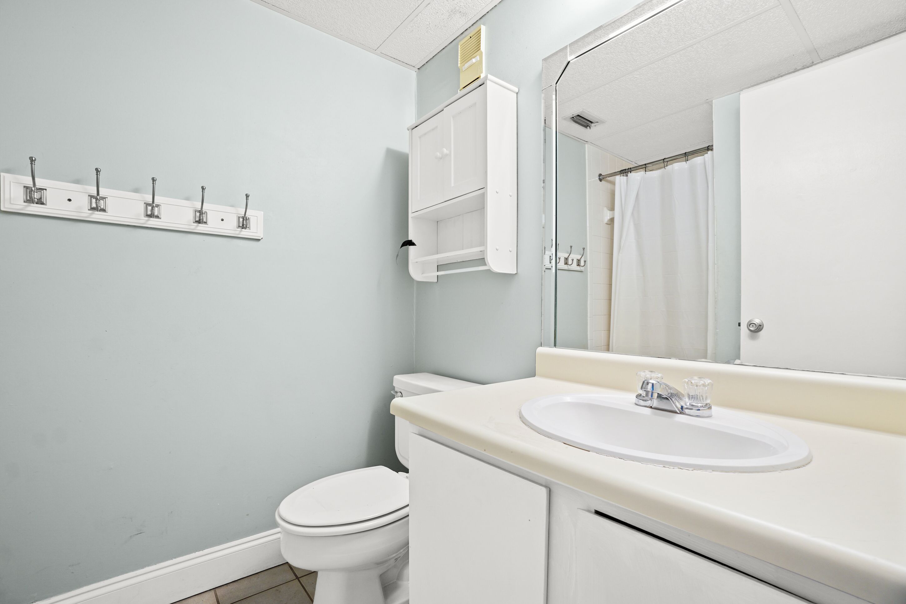 A bathroom with a white toilet, a sink with a mirror above it, and a towel rack on the wall.