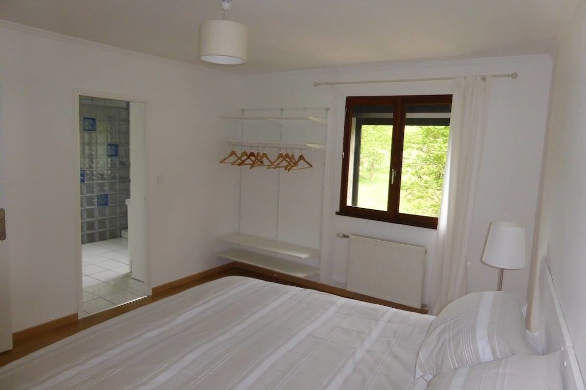 Ein Schlafzimmer mit Bett, Fenster, Heizkörper und einer Kleiderstange.