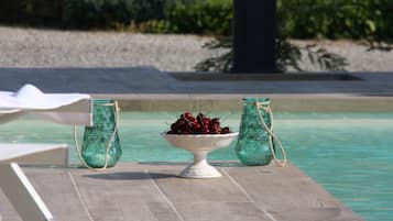 Ein Tisch am Pool mit einer weißen Schüssel voll Kirschen und zwei grünen Glasflaschen, die mit Bindfaden verbunden sind.