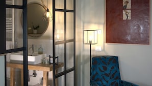 Une pièce avec un plancher en bois, une chaise bleue à motifs, un lavabo blanc et un grand tableau abstrait accroché au mur.
