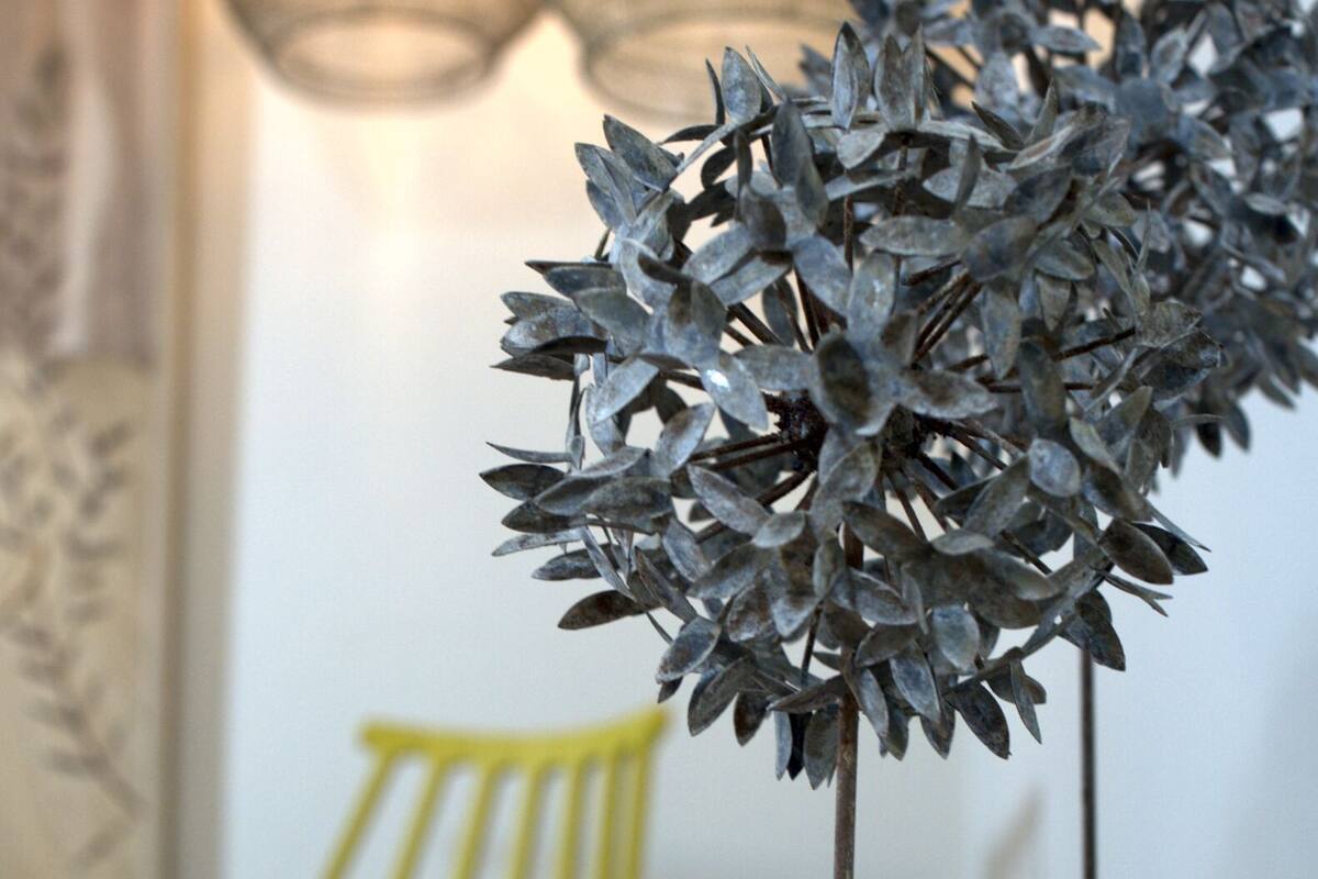 Une sculpture en métal est posée sur une table en bois, avec une chaise jaune et un livre en arrière-plan.