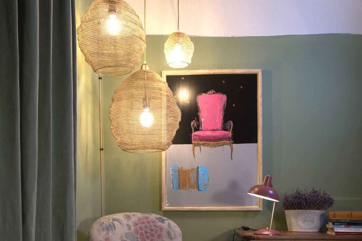 Une pièce comprenant un fauteuil à motifs floraux, une commode en bois, un tableau encadré et un luminaire en fibres tressées.