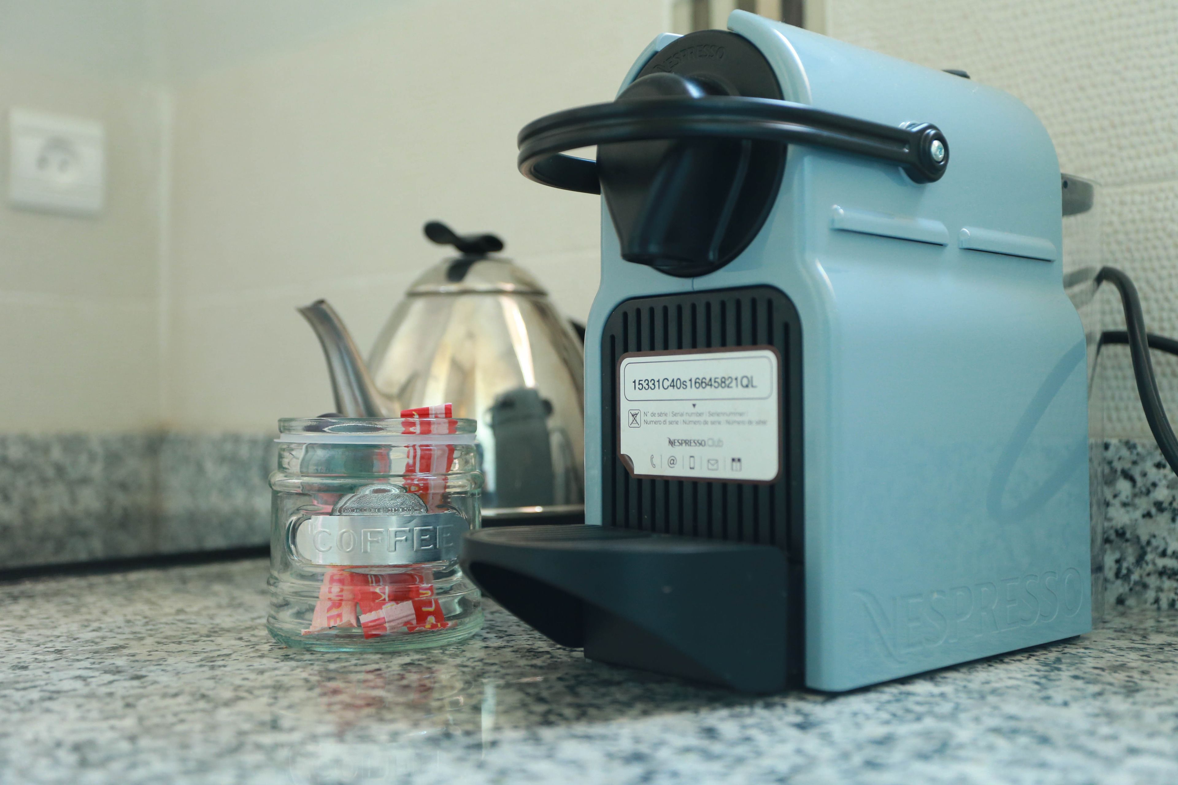Una máquina de café Nespresso sobre una encimera de cocina, junto a un tarro de vidrio con cápsulas de café.