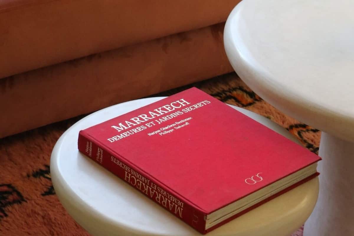 A red book titled 'Marrakech Demerets Et Jardins Secrets' on a white pedestal table.