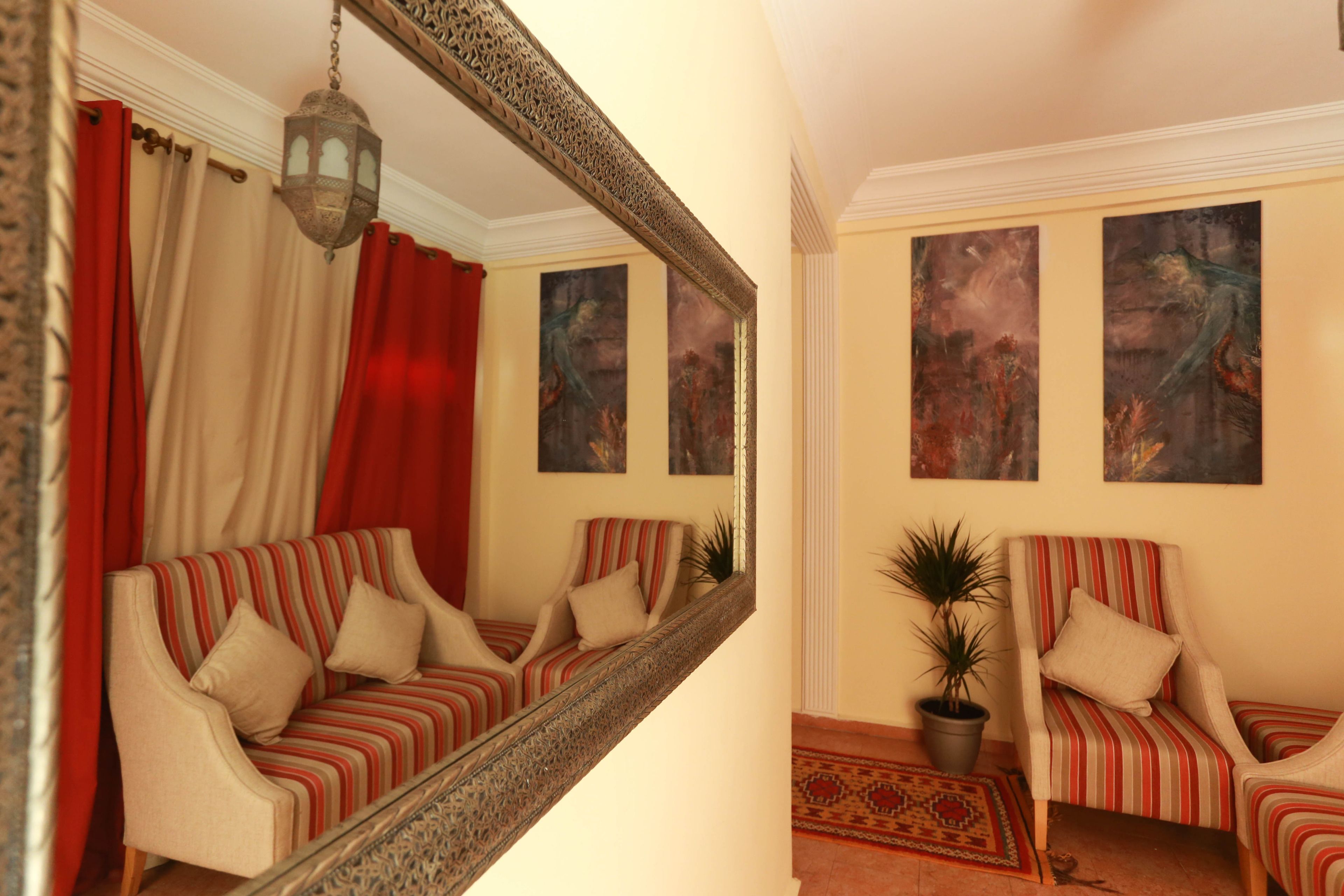 Une pièce comprenant un canapé et des fauteuils, un grand miroir et deux tableaux accrochés au mur.