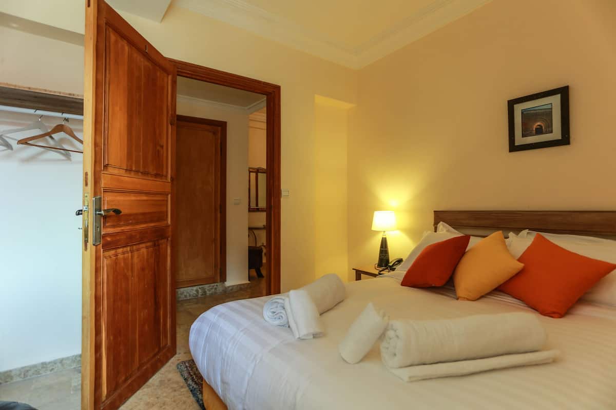 A hotel room with a bed, towels, pillows, a lamp, and a framed picture on the wall.
