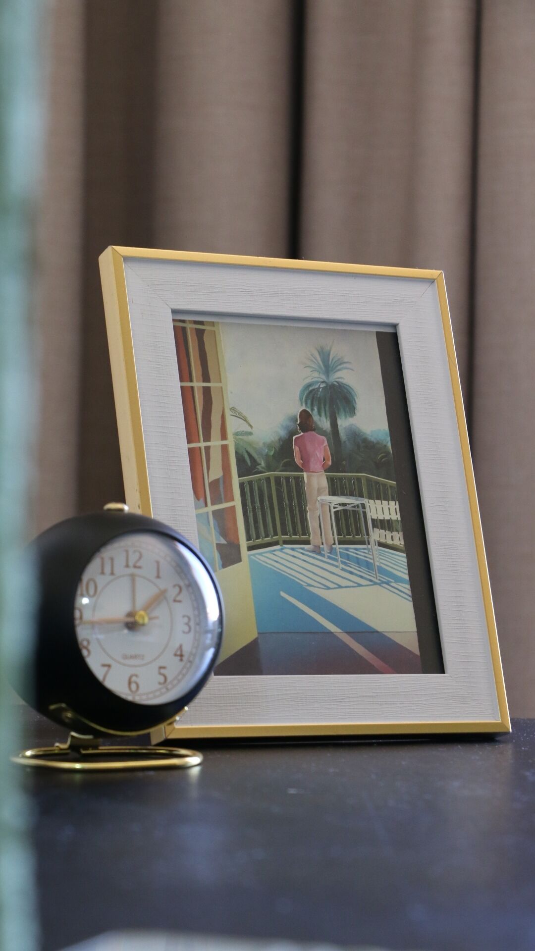 Una fotografia emmarcada d'una dona en un balcó, amb un rellotge a prop.