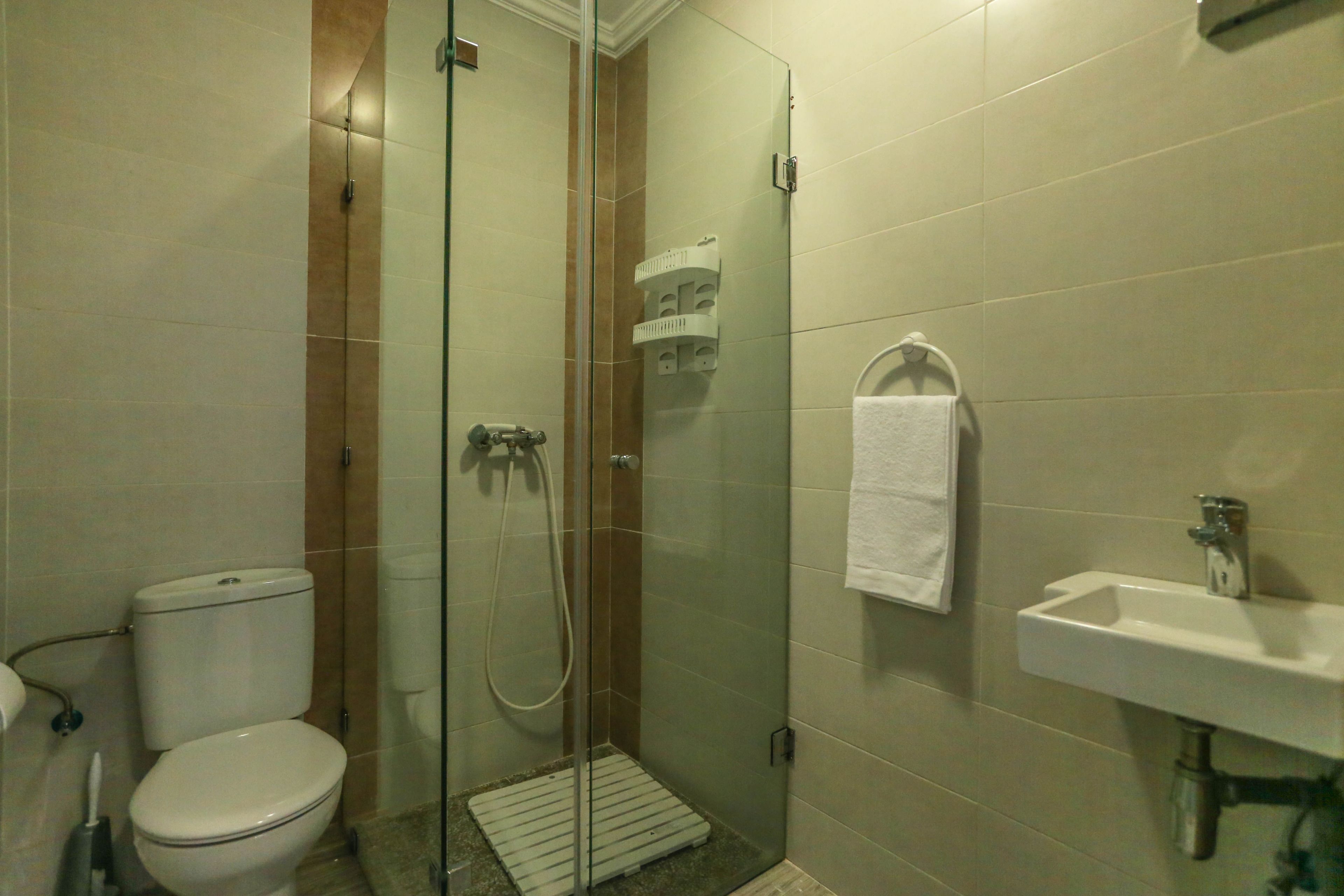 Un baño con inodoro, ducha con mampara de vidrio y lavamanos con una toalla colgada en la pared.